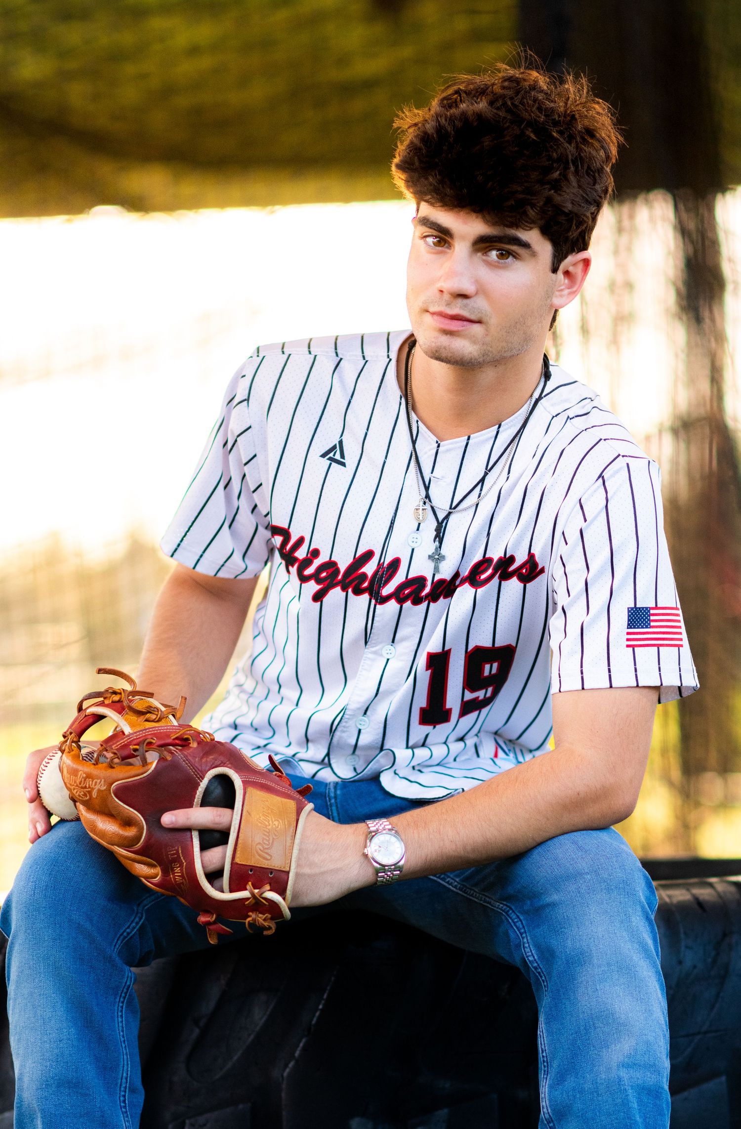 High school senior in Highlanders baseball jersey number 19 holding glove at golden hour.