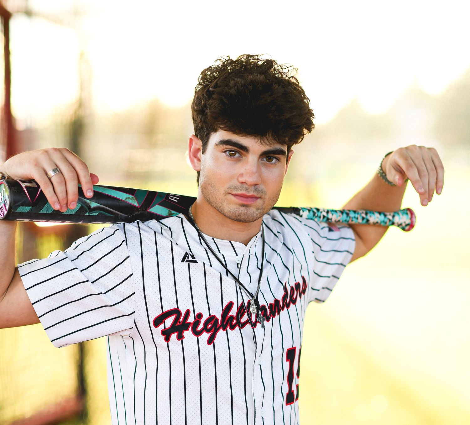 Young baseball player in Highlanders jersey posing with bat on field.
