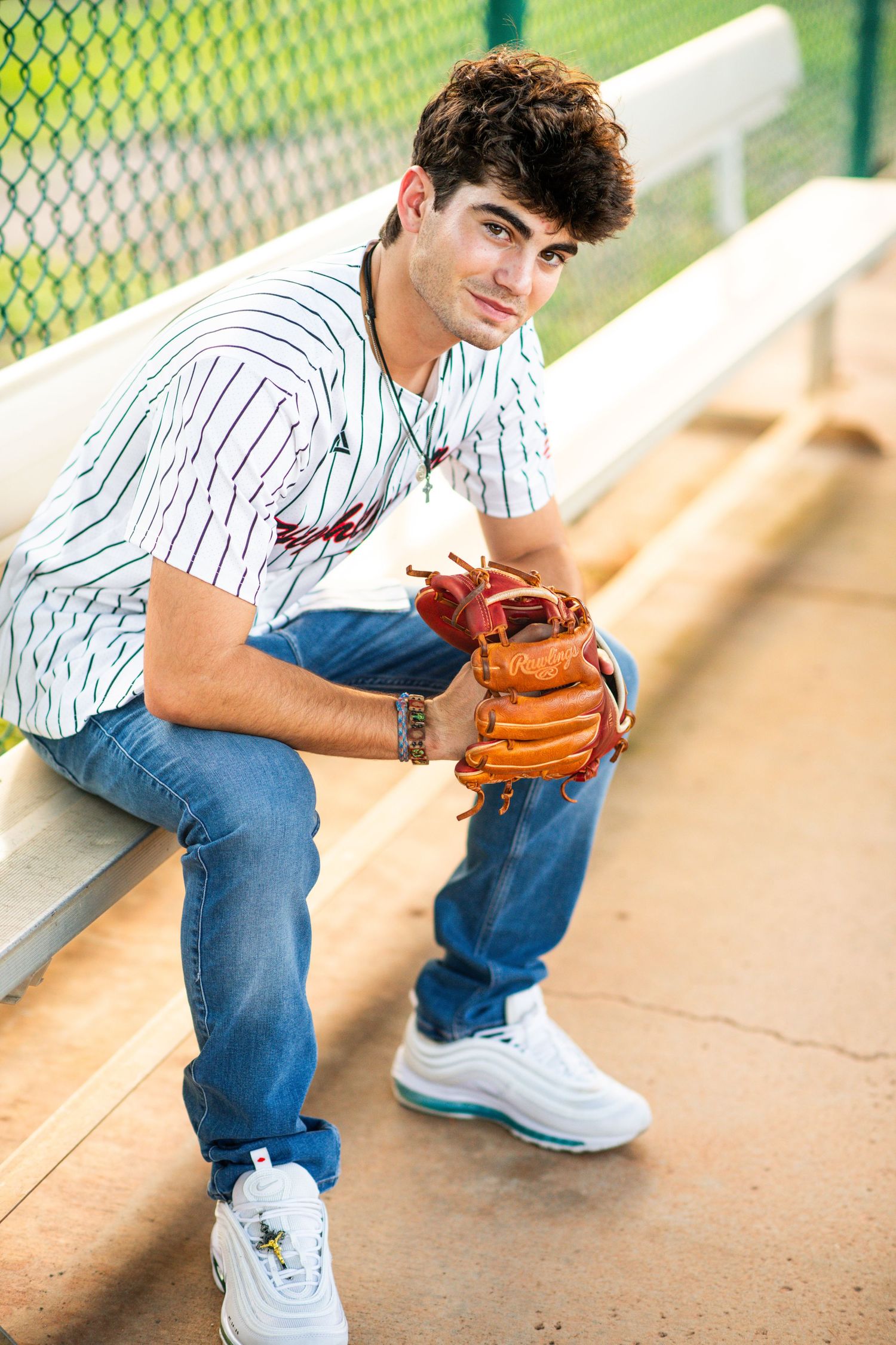 Teen baseball player sitting in dugout holding glove and ball.