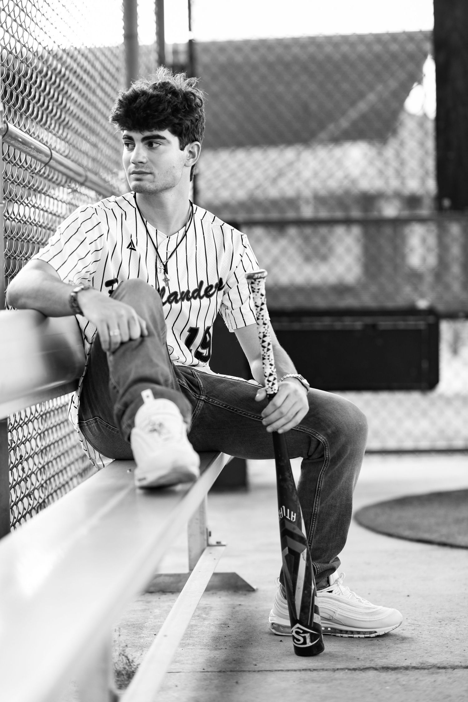 Young male baseball player sitting in dugout holding bat in black and white photo.