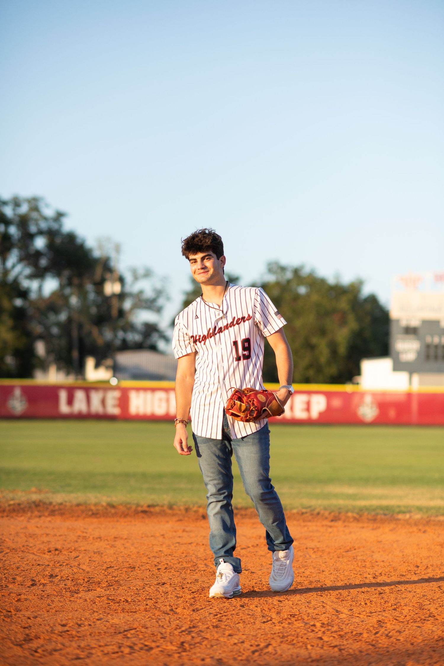 Baseball player in Highlanders jersey number 19 standing on baseball field at sunset.