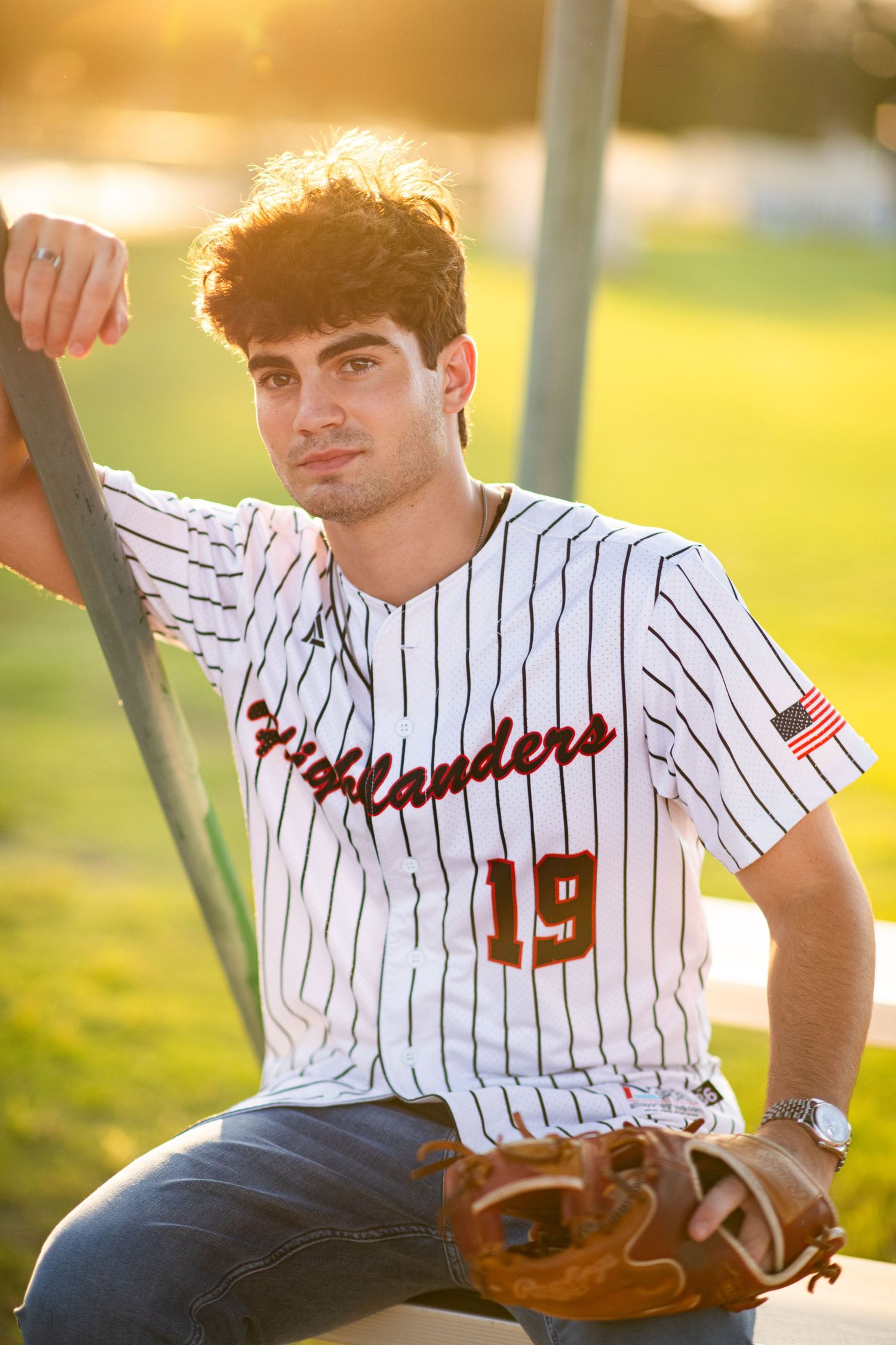 Teen baseball player in Highlanders number 19 jersey with glove posing at golden hour.