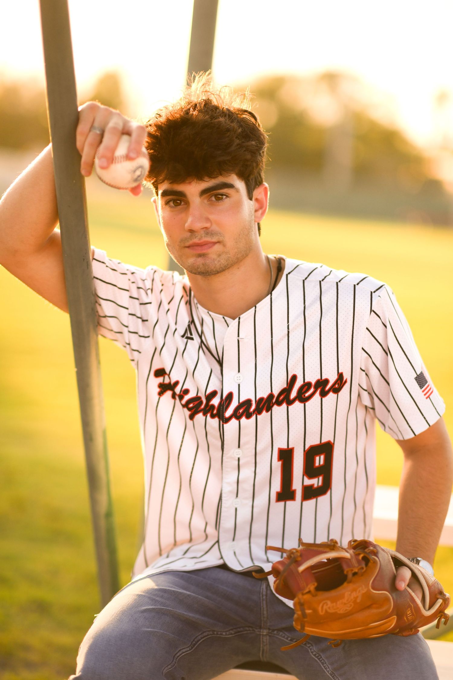 Young man in Highlanders number 19 jersey holding baseball glove at sunset.