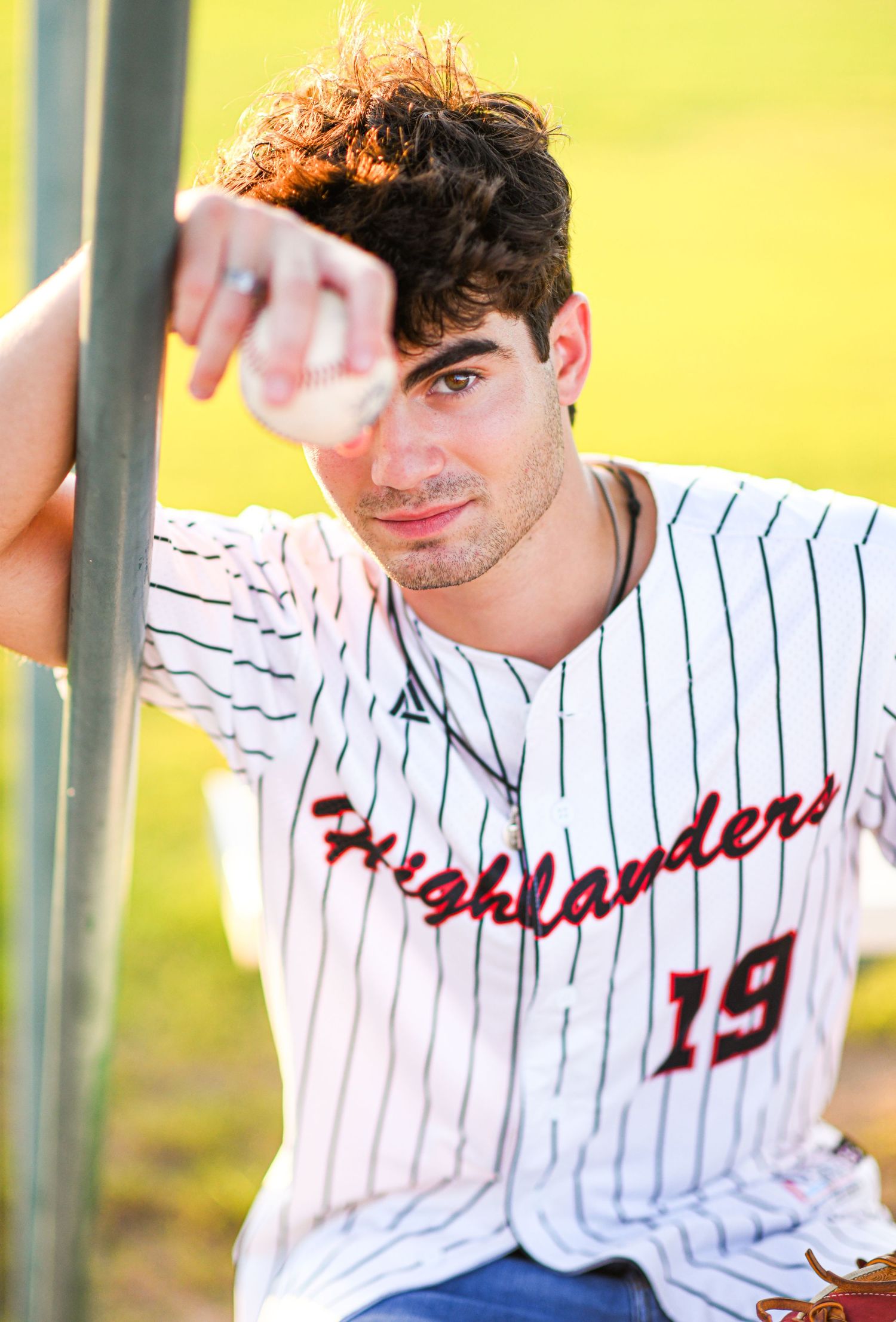 Young baseball player in Highlanders number 19 jersey posing against fence on field.