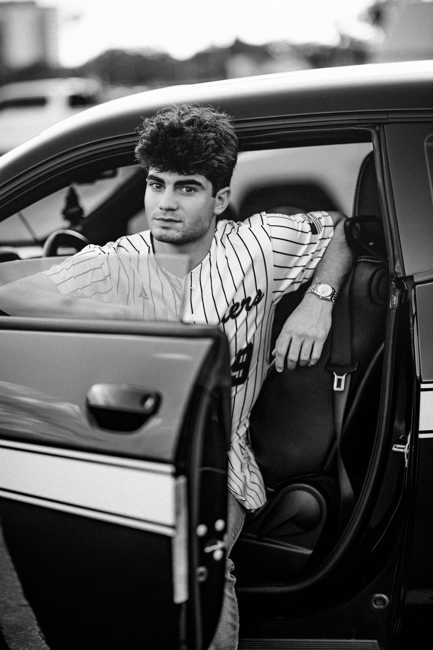 Young man in striped baseball jersey leaning out of car door in black and white portrait photo.
