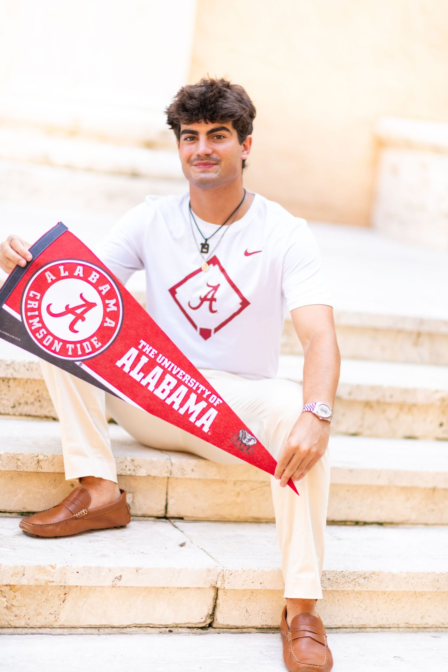 Young man sitting on steps holding University of Alabama pennant wearing Crimson Tide shirt.