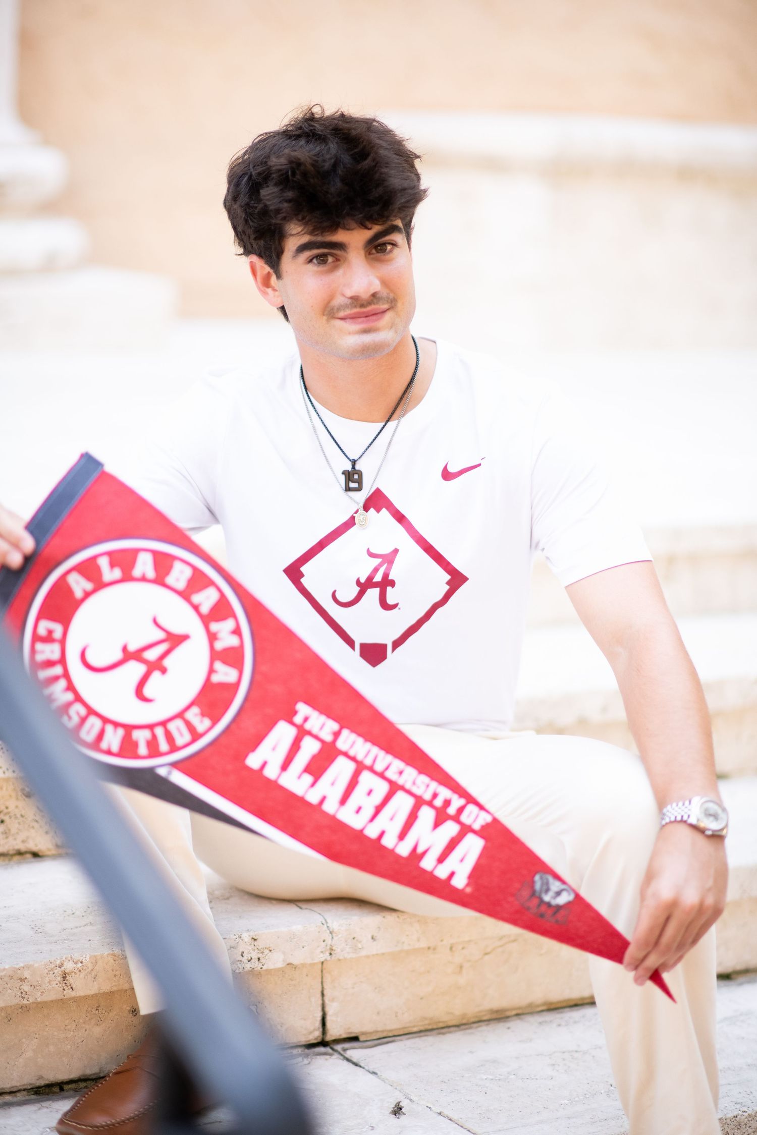 Young man in Alabama Crimson Tide shirt holding University of Alabama pennants on steps.