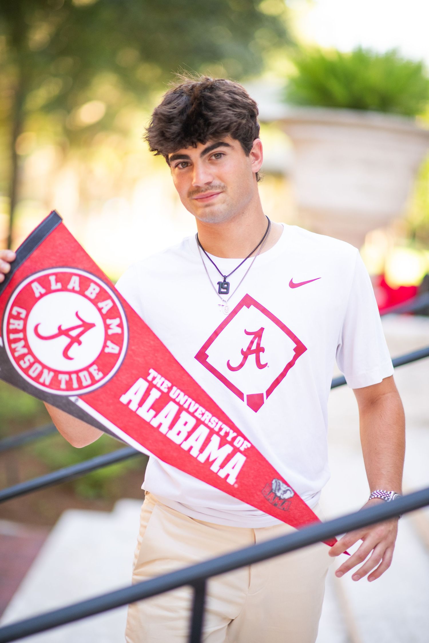 Young man holding University of Alabama pennant wearing Crimson Tide shirt outdoors.
