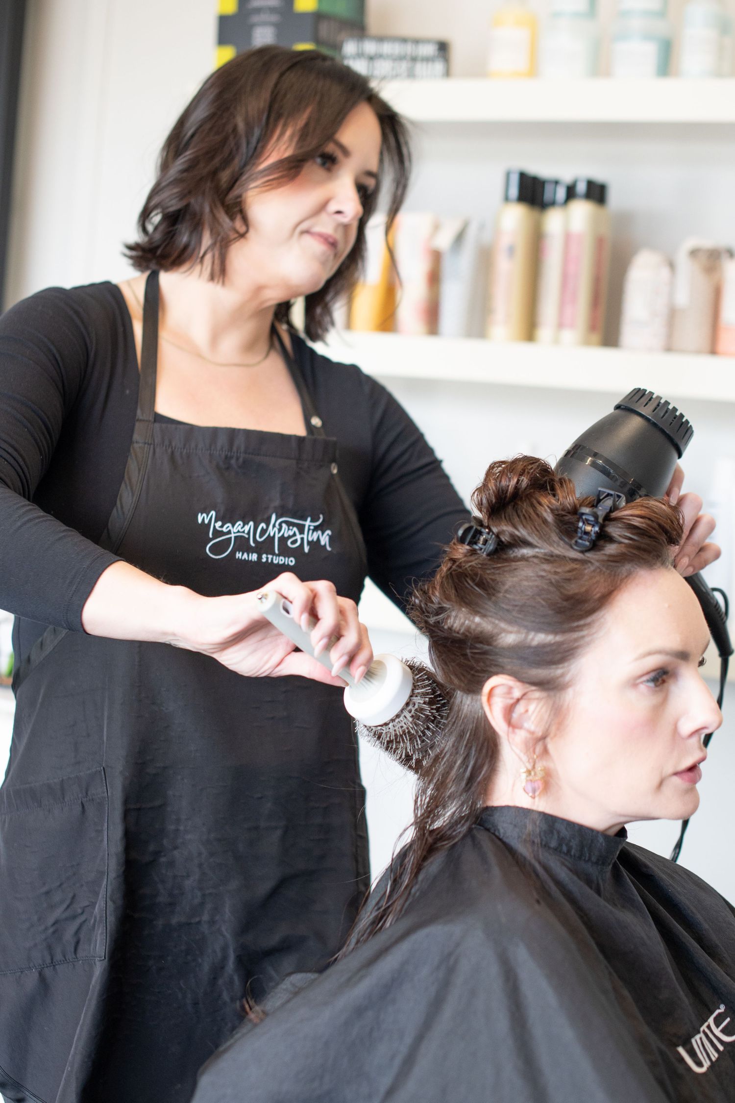 Female hairstylist blow drying a client's hair in a professional salon setting.