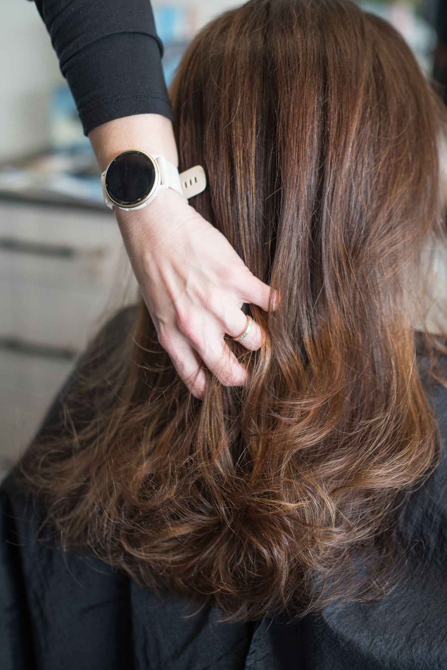 Hairstylist wearing a smartwatch clips brown hair during a salon styling session.