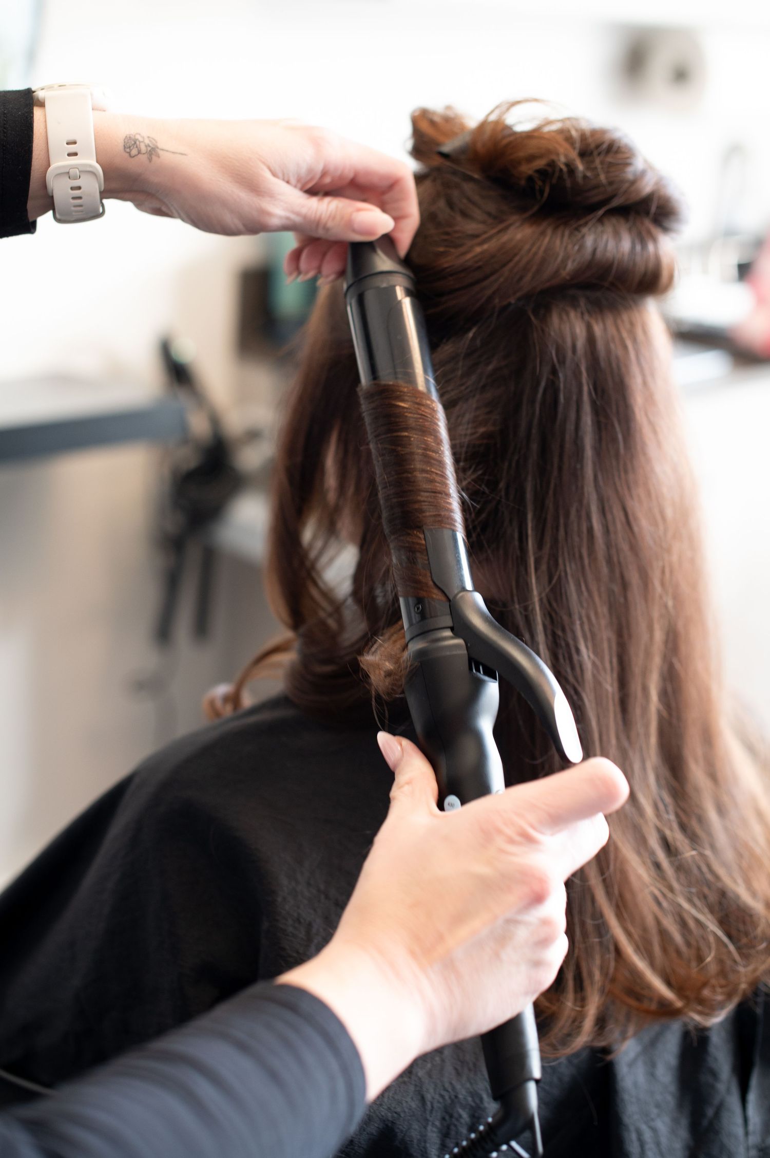 Hairstylist using a curling iron on brunette hair in a salon.