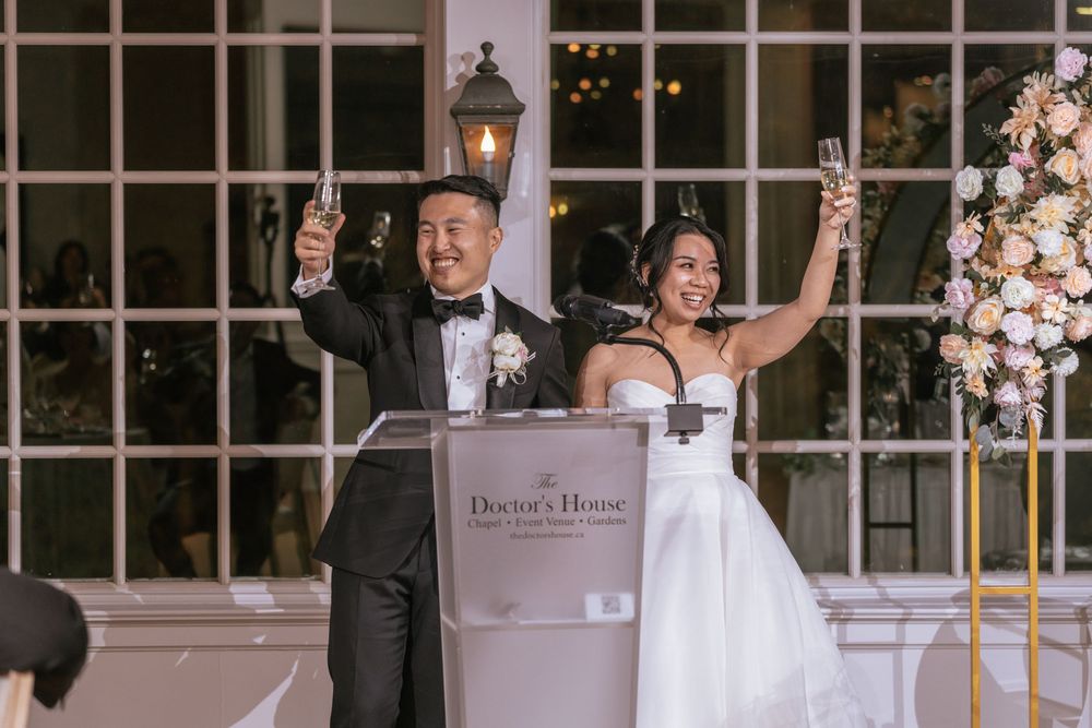 Bride and groom raising champagne glasses at The Doctor's House wedding reception, smiling joyfully.