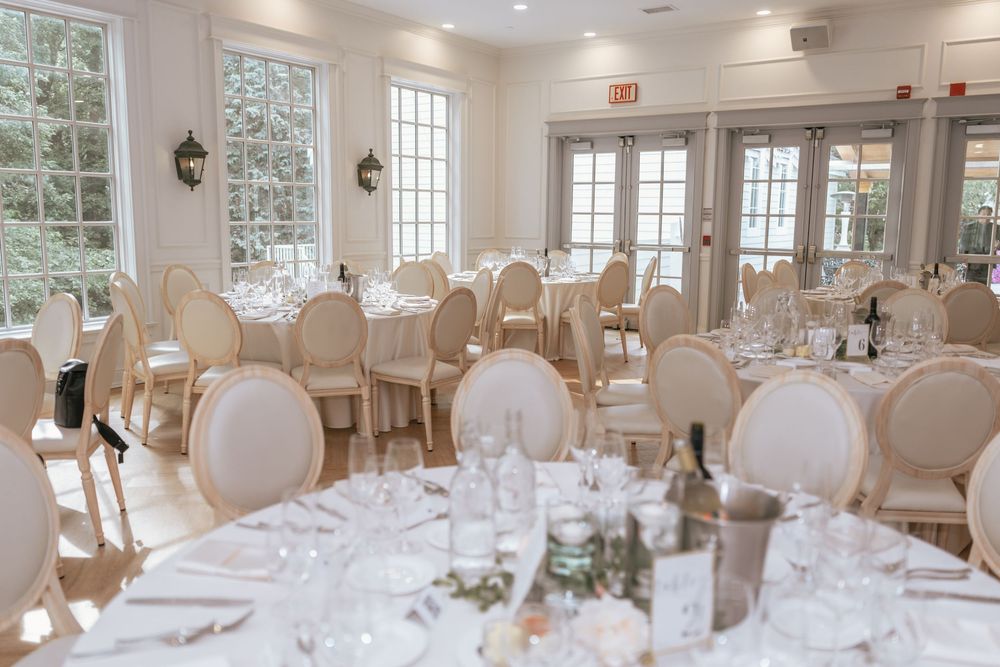 Elegant wedding reception hall with ivory chairs, white linen tables, and natural light from large windows.