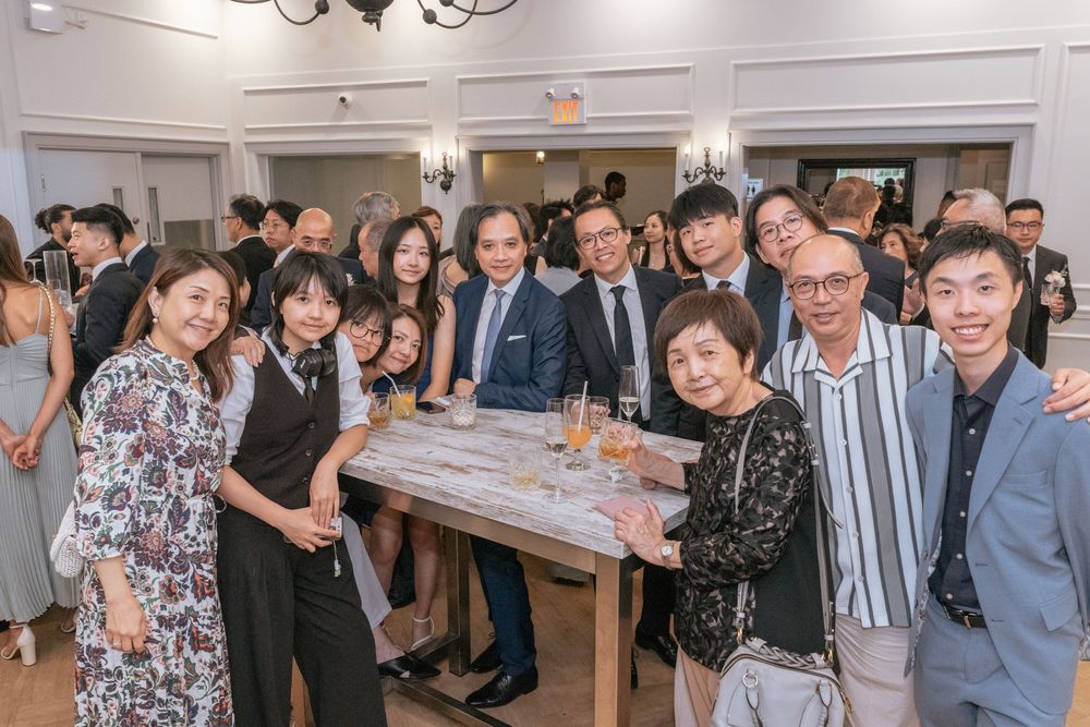 A large group of elegantly dressed guests smiling together at a formal event or wedding reception indoors.