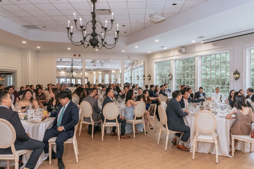 Elegant wedding reception hall filled with guests seated at round tables under a chandelier.