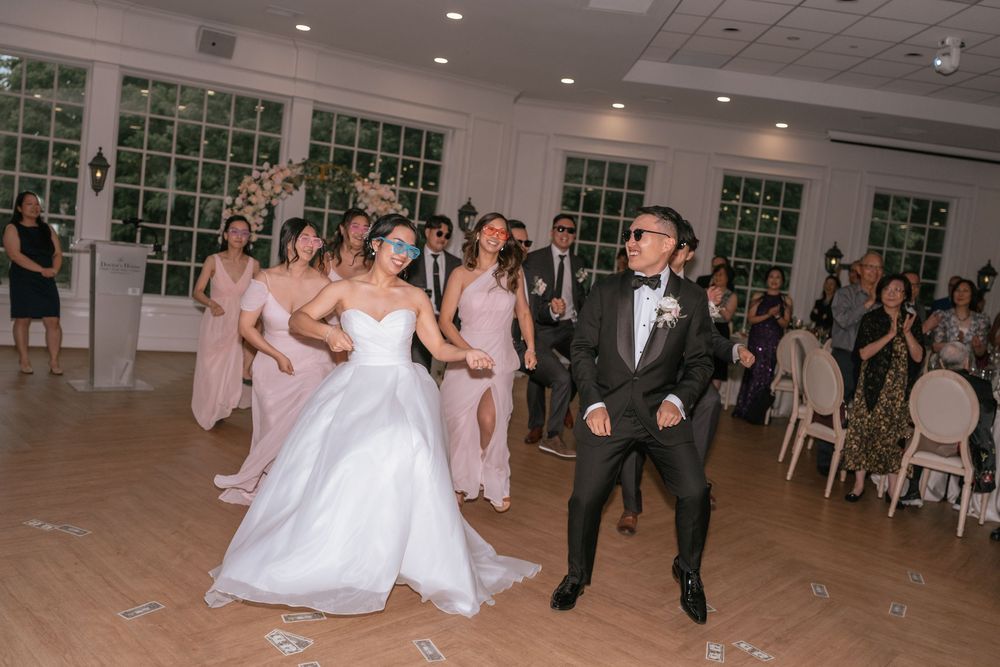 Bride and groom share a joyful first dance surrounded by bridesmaids in pink dresses at an elegant wedding reception.