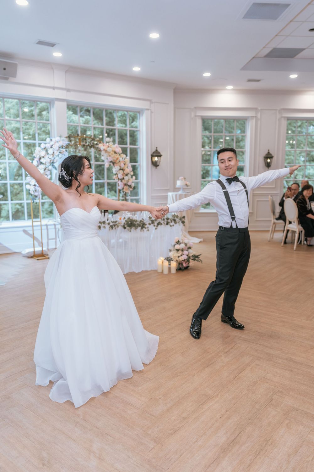 Bride and groom share their first dance in an elegant white ballroom during their wedding reception.