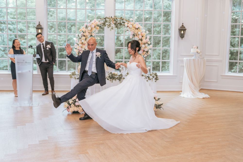 Bride and groom share first dance under floral arch in elegant white ballroom during wedding reception.
