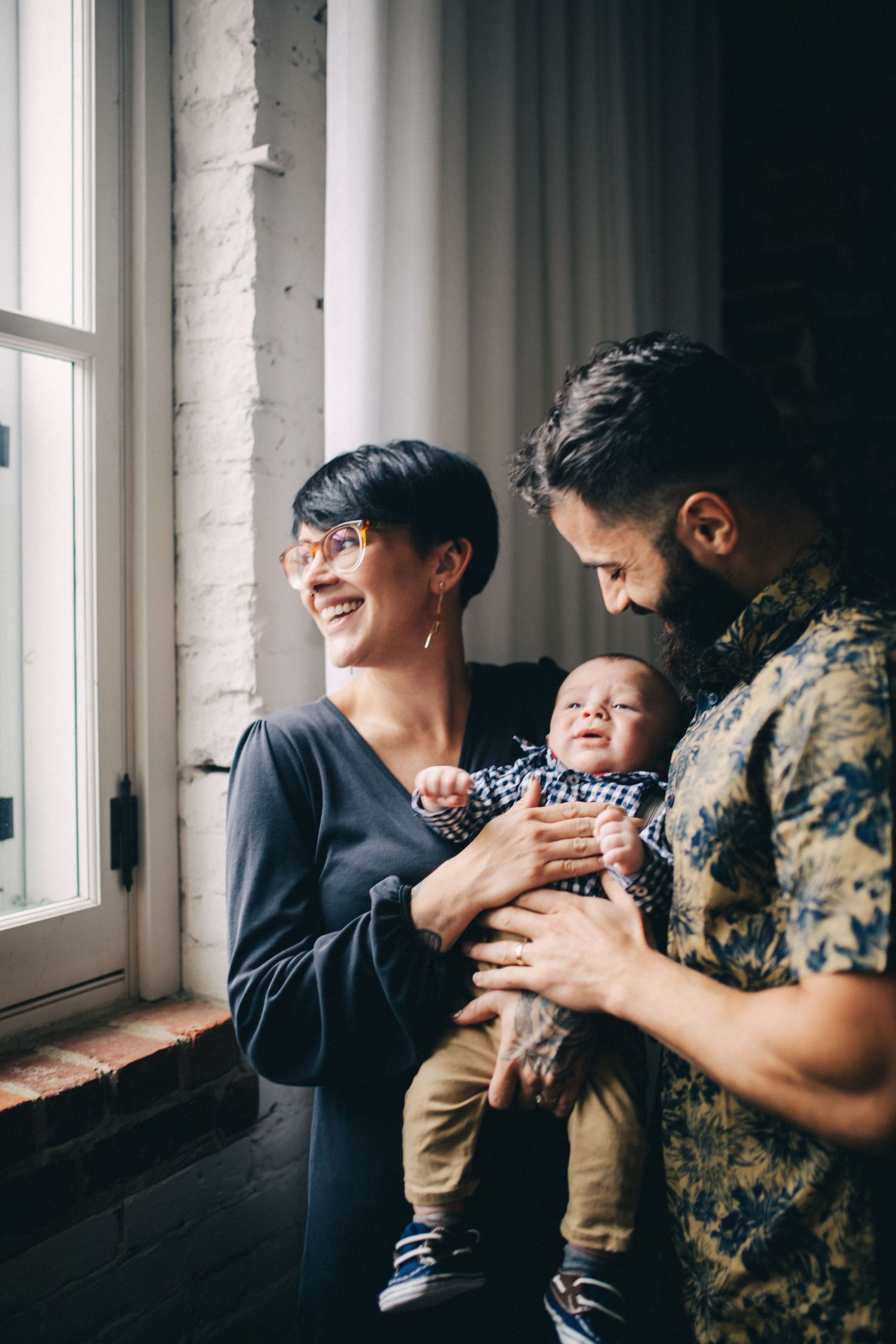 Family sharing a tender moment by a bright window in an industrial-style loft space.