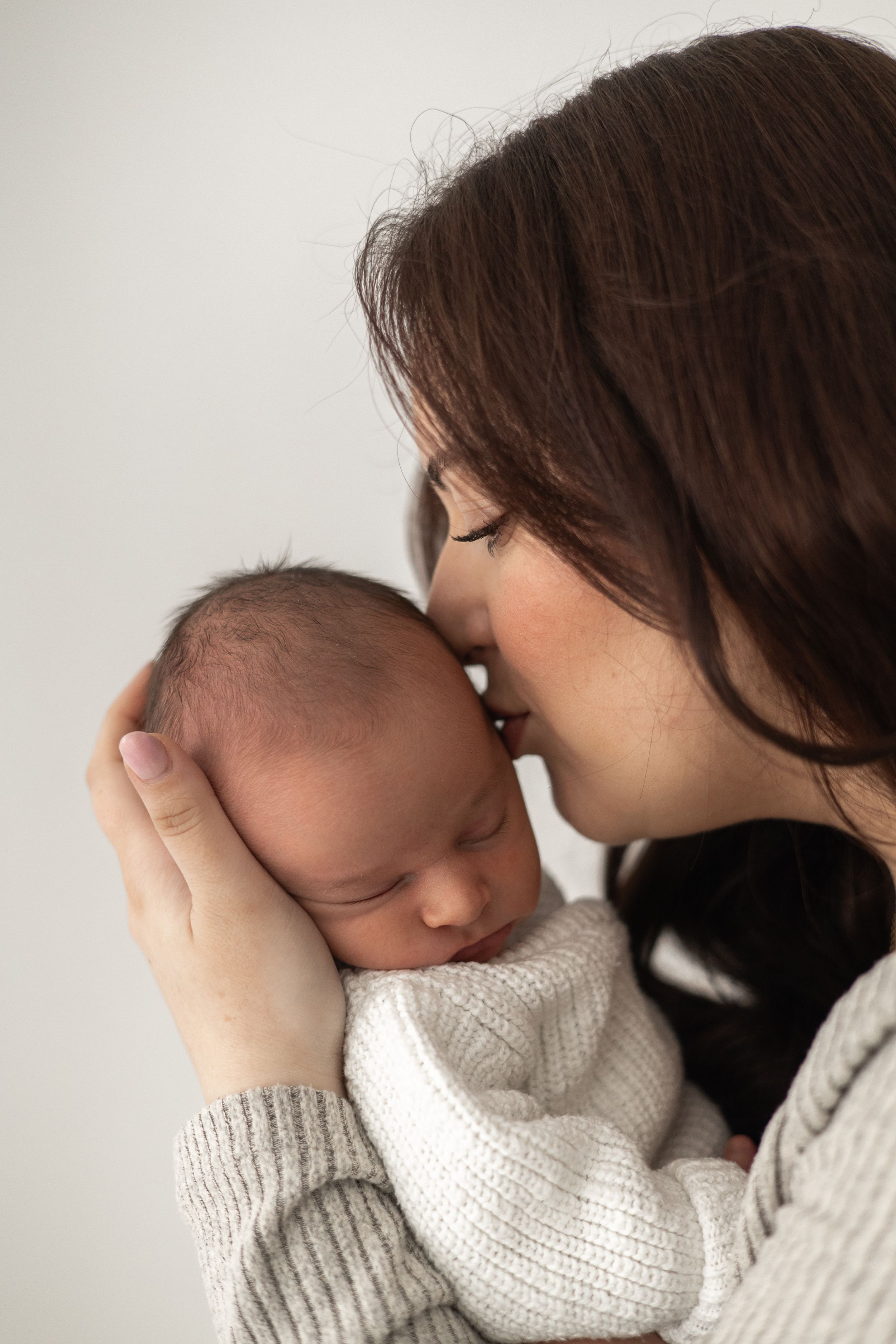 A mother tenderly kisses her sleeping newborn baby, cradling baby gently in her hands Nottingham newborn photographer