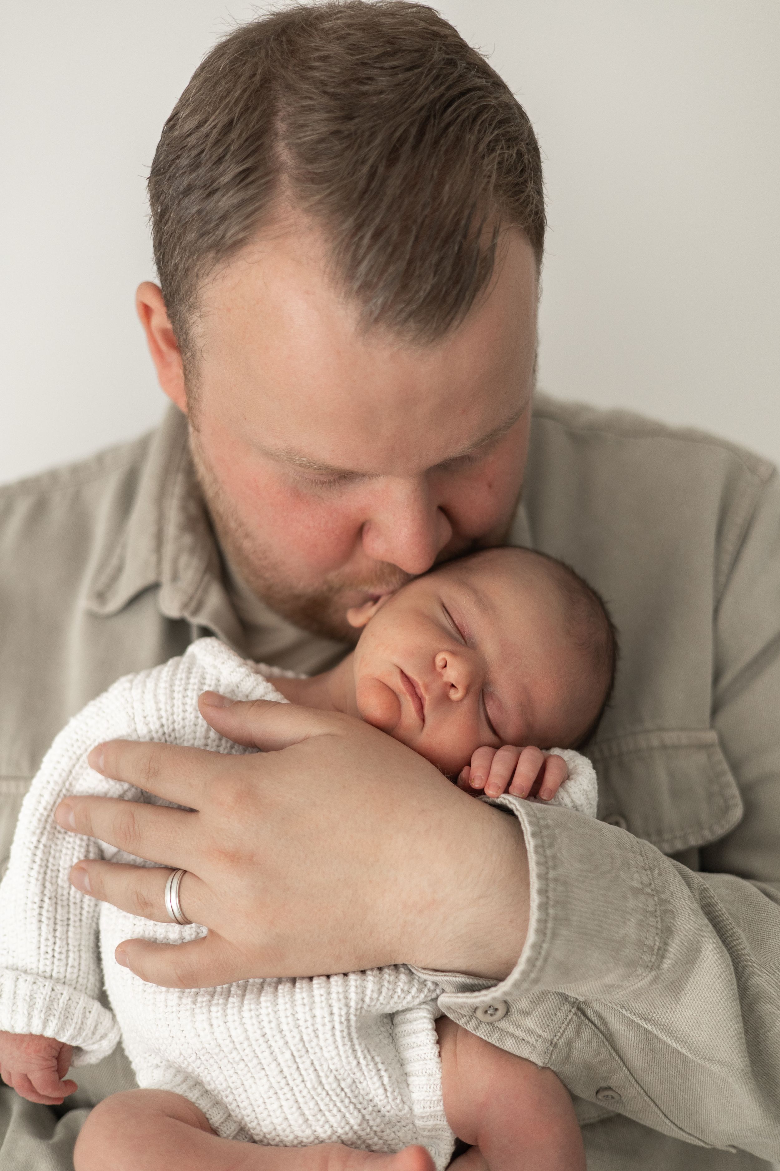 A dad tenderly kisses his sleeping newborn baby dressed in white, timeless Nottingham newborn photographer