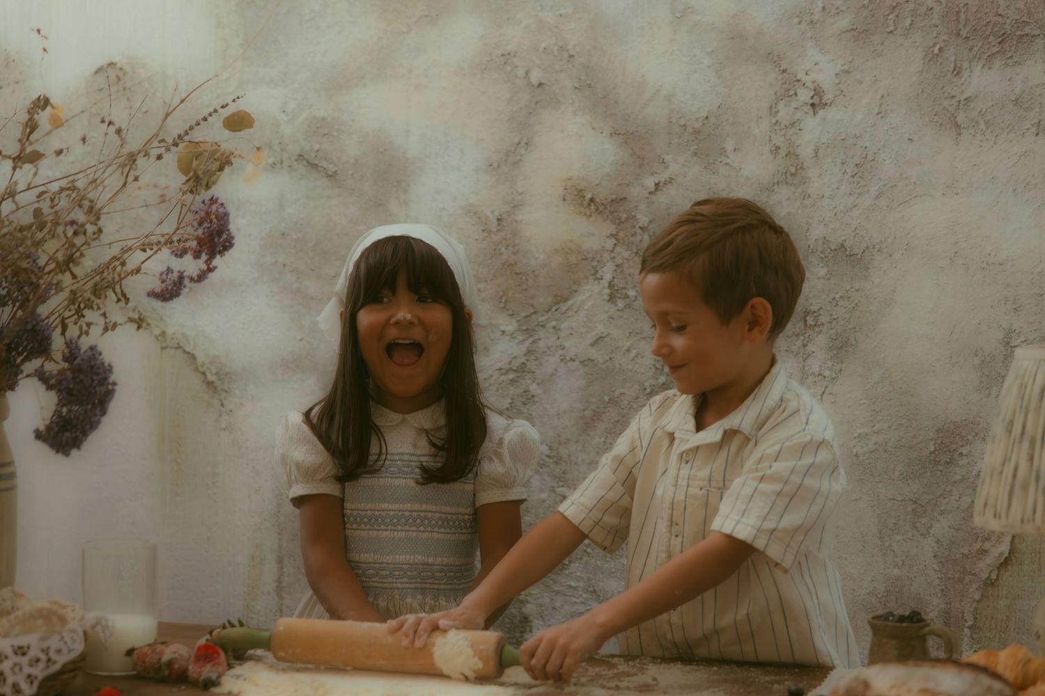 An Orange County family photographer captures two children joyfully rolling dough together at a table, with dried flowers in the background.