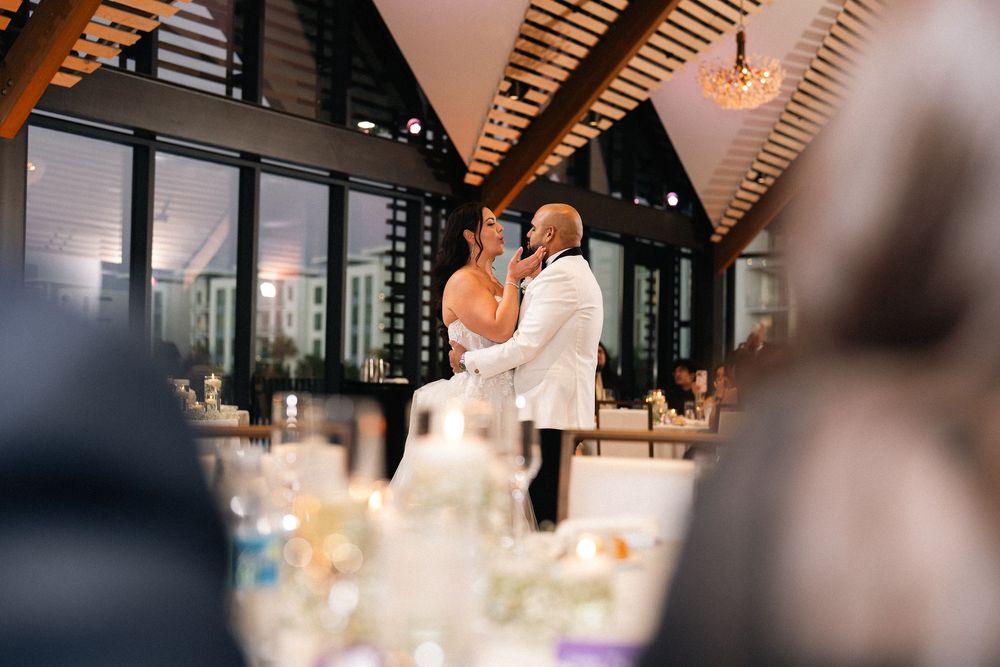 Couple shares first dance at elegant wedding reception with wooden ceiling and large windows.