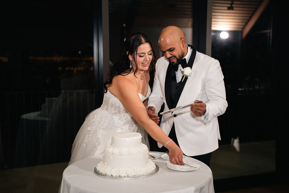 Bride and groom cutting their white wedding cake together at a nighttime reception.