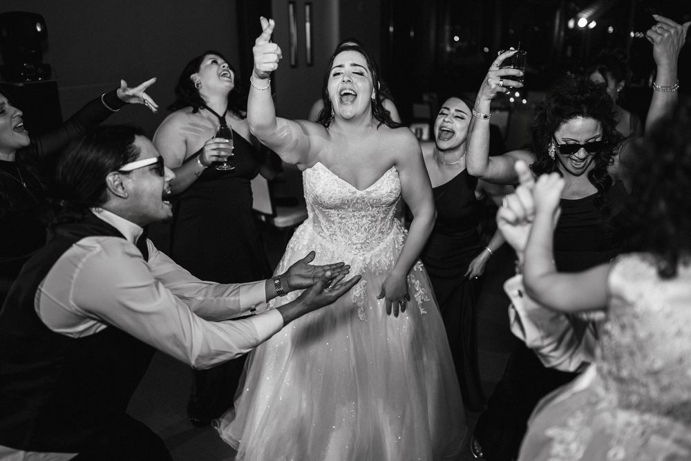 Bride joyfully dancing with guests at a lively black and white wedding reception.