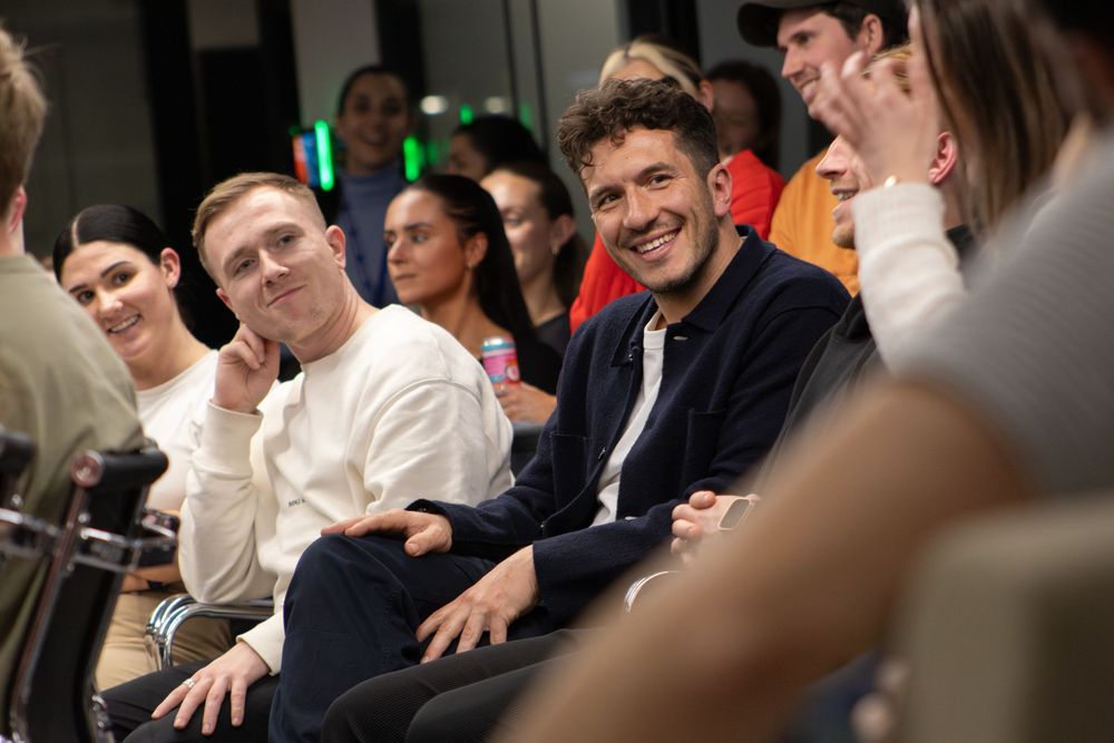 Group of smiling people sitting together at an indoor event, engaged in conversation in a modern venue.
