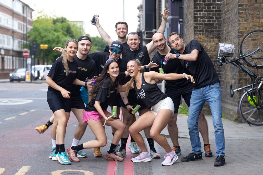 Group of friends posing energetically on a London street, wearing black athletic wear, celebrating together outdoors.