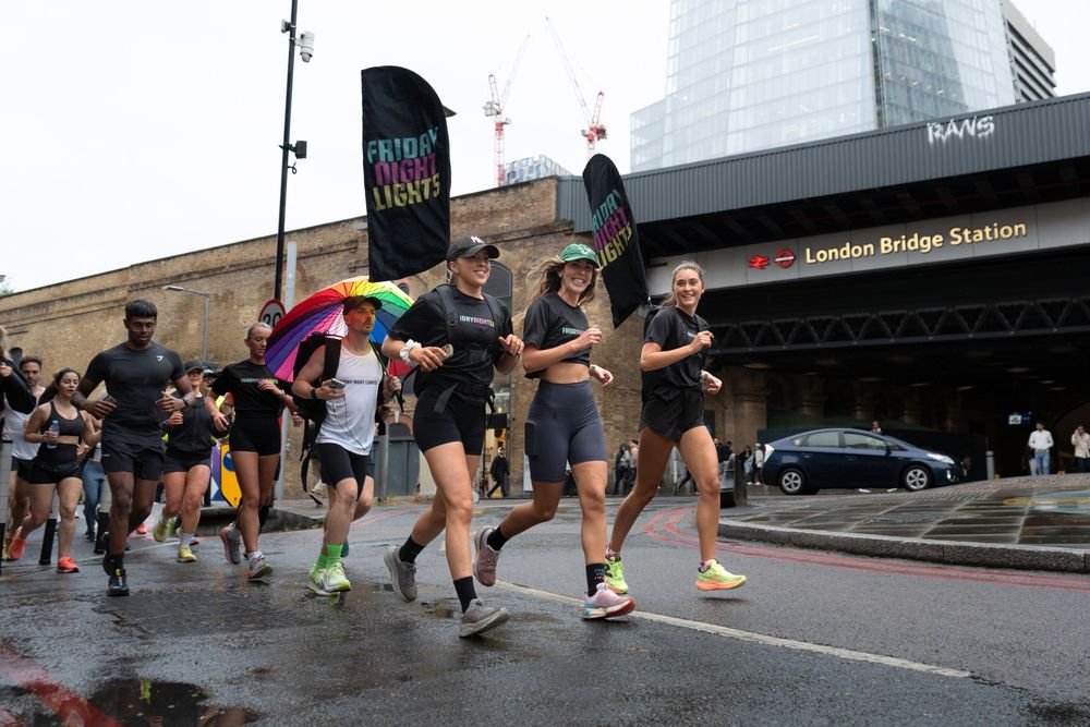 Runners jogging past London Bridge Station during a group run event on a rainy day.