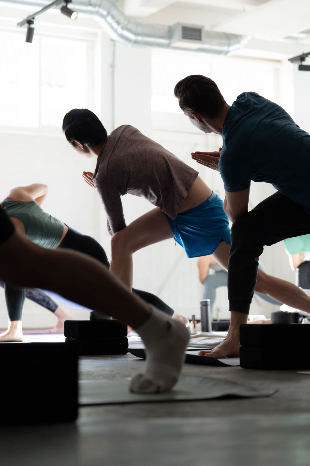 Group of people practicing yoga poses on mats in a bright modern studio during a fitness class.