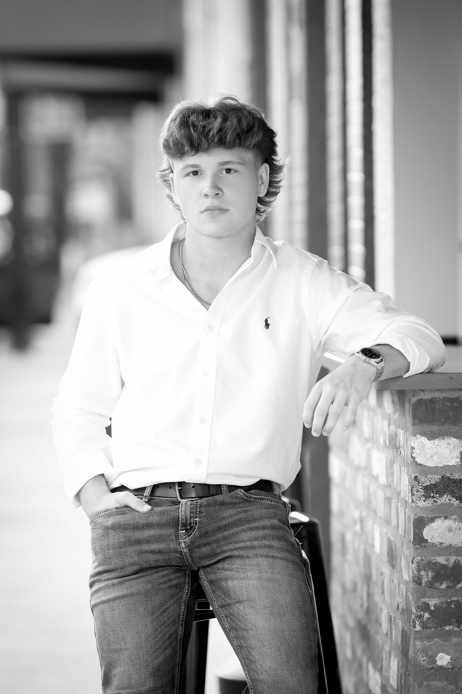 Black and white portrait of a teenage boy in a white Polo shirt and jeans leaning against a brick wall outdoors.