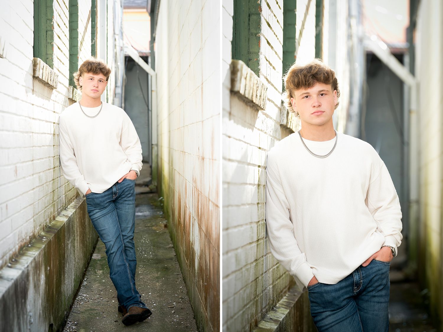 Teen boy in white sweater and jeans posing in a narrow alley between brick walls for senior photos.