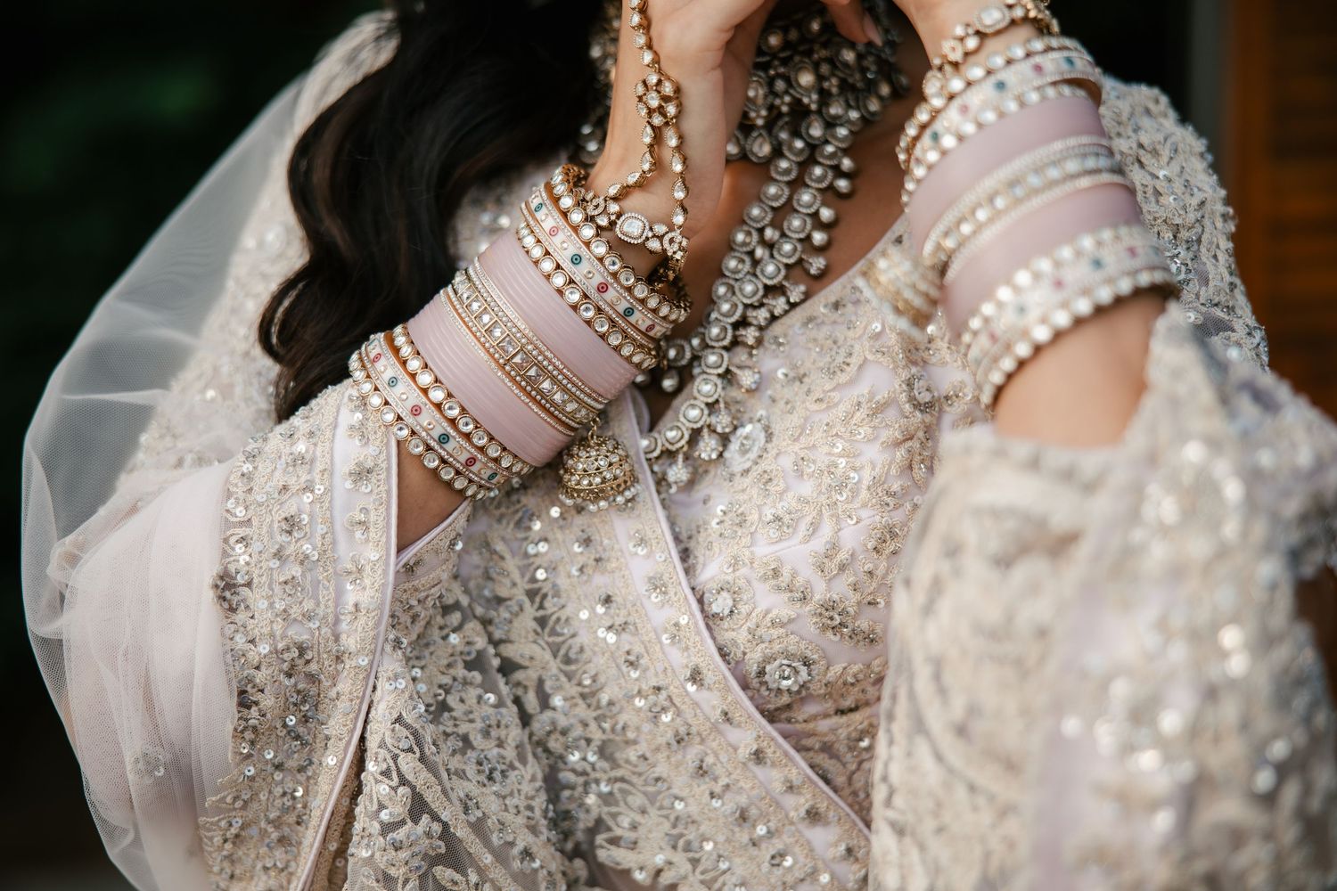 South Asian bride in embellished white lehenga adorned with silver bangles and pearl jewelry at wedding.