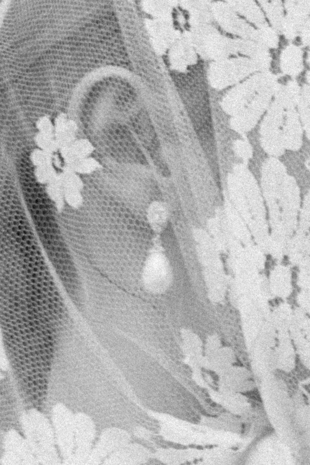 Close-up of a bride wearing a pearl drop earring with floral stud, framed by delicate lace veil.