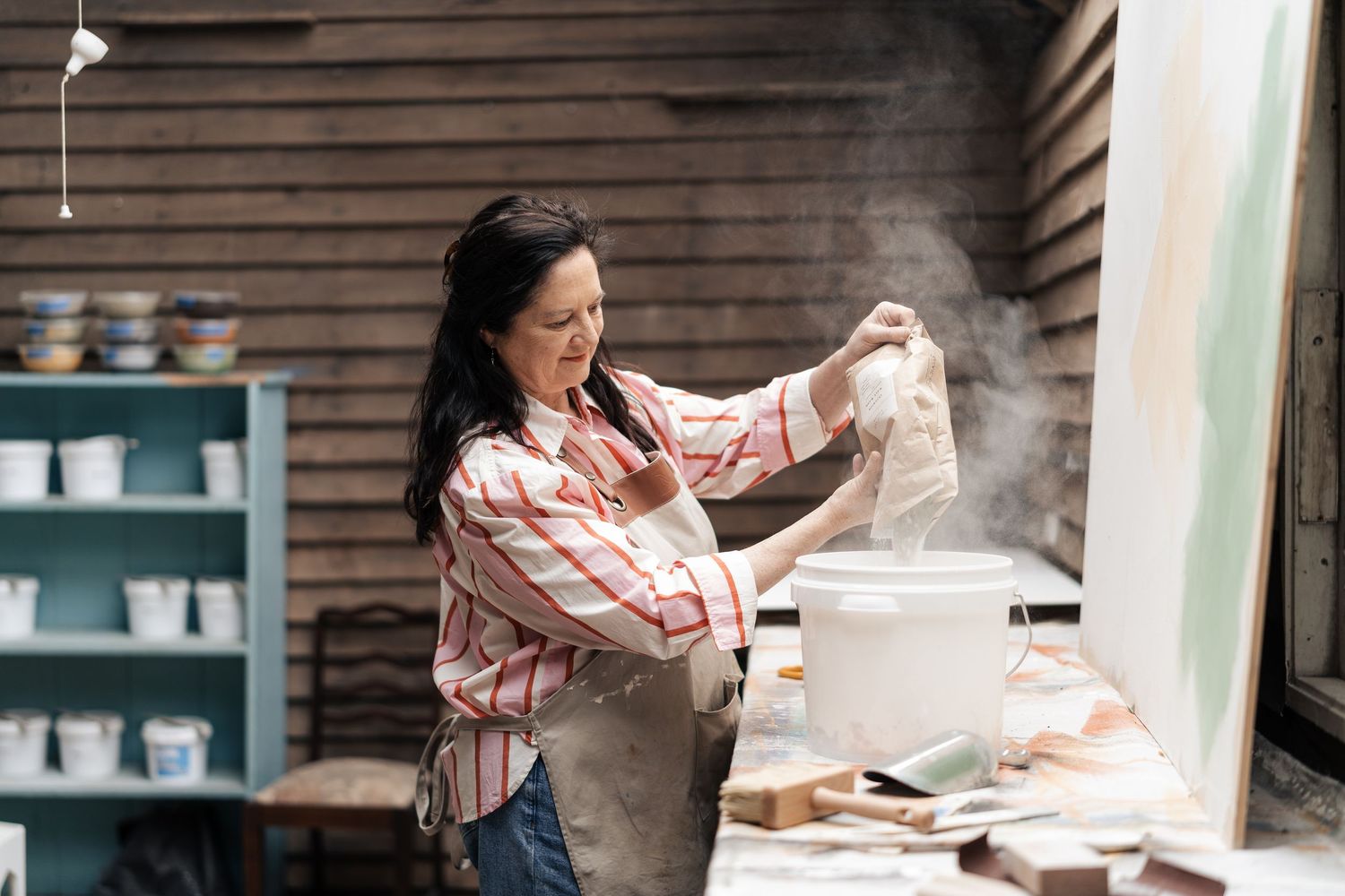 A dark-haired woman in a plaid shirt works with clay materials in a rustic pottery studio.

Lime Au Lait Atelier