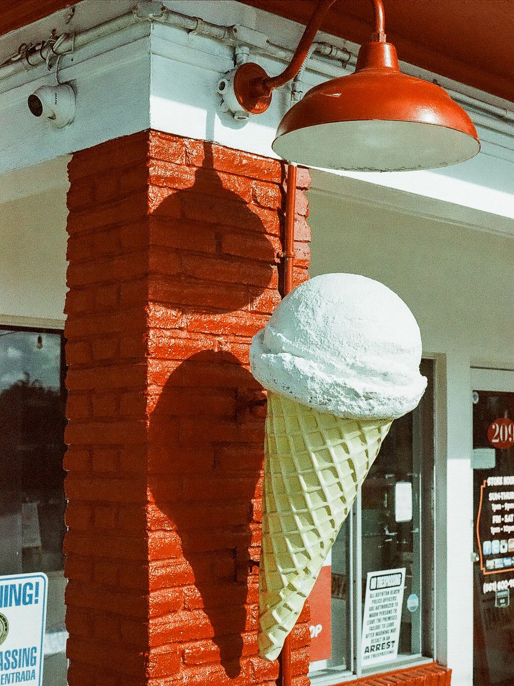 Large decorative ice cream cone sign on a red brick pillar outside a vintage ice cream shop.