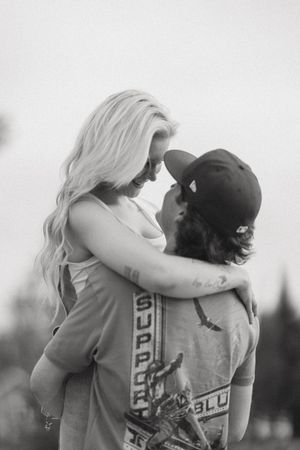 Black and white photo of a couple embracing and touching foreheads romantically outdoors.
