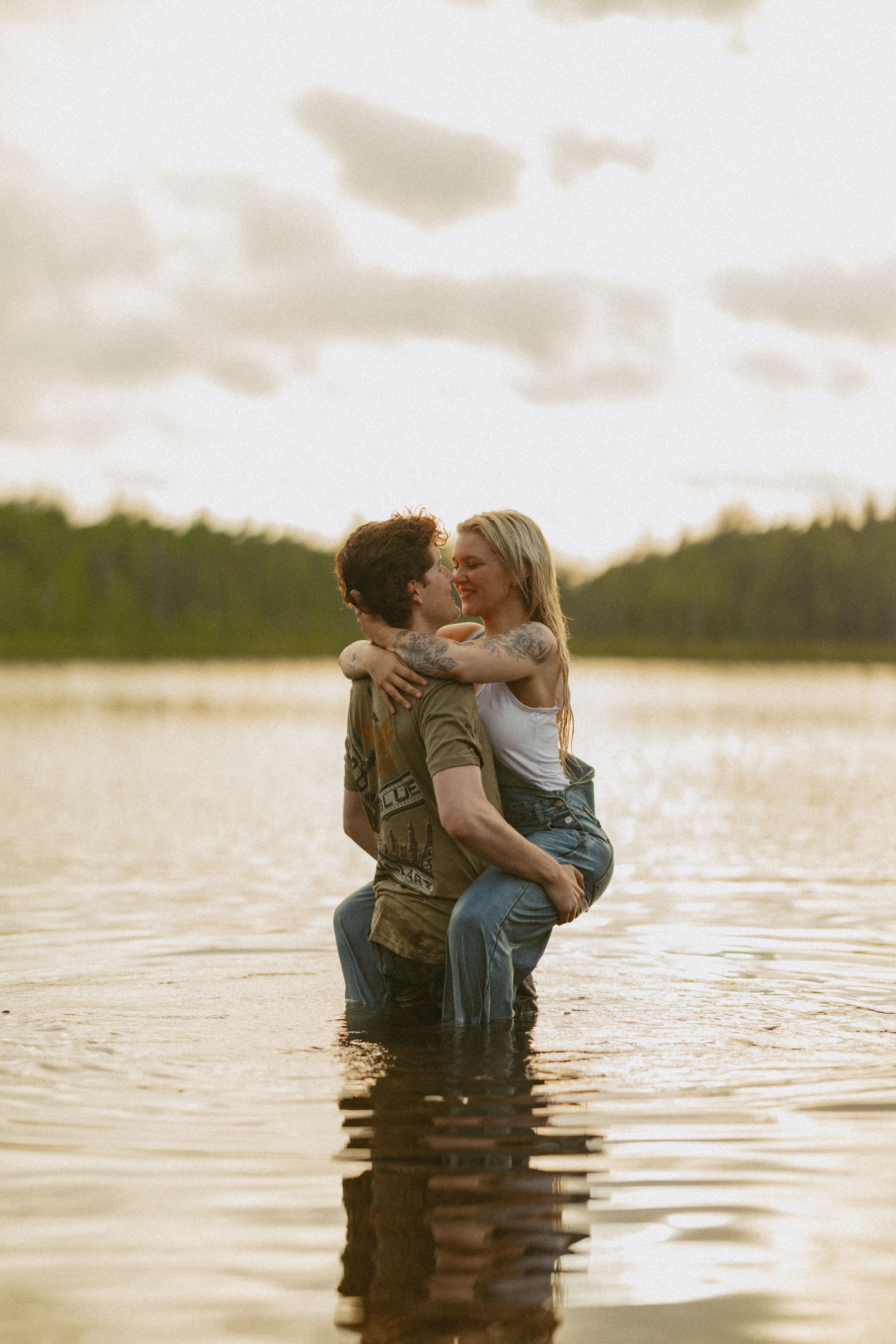 Romantic couple kissing while standing in a lake at golden hour sunset.