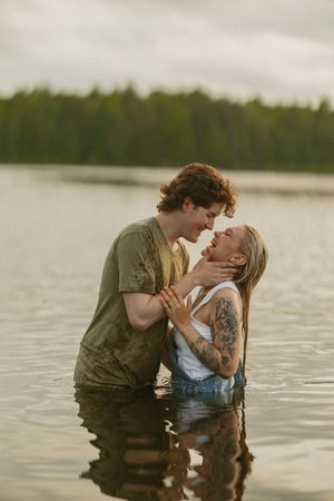 Romantic couple standing chest-deep in calm lake water, leaning in for a kiss at dusk.