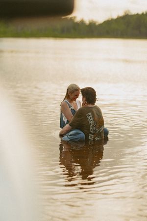 Couple sitting together in a shallow golden lake at sunset, sharing an intimate moment surrounded by nature.