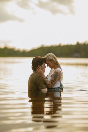 Couple embracing forehead to forehead while standing together in a calm lake at sunset.