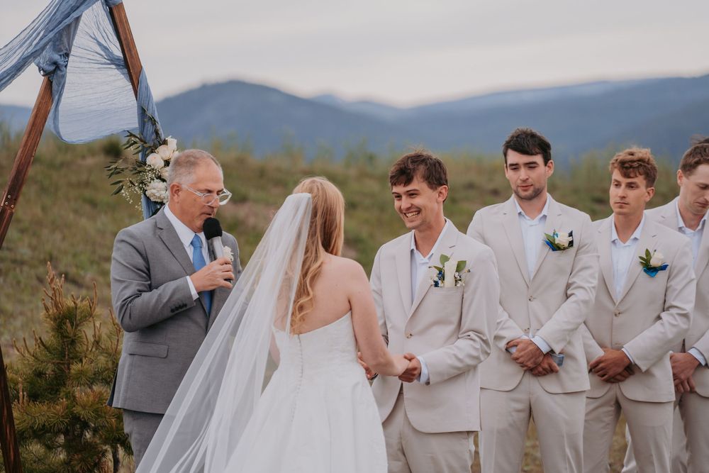 Bride and groom exchange vows at an outdoor mountain wedding ceremony with groomsmen and officiant.