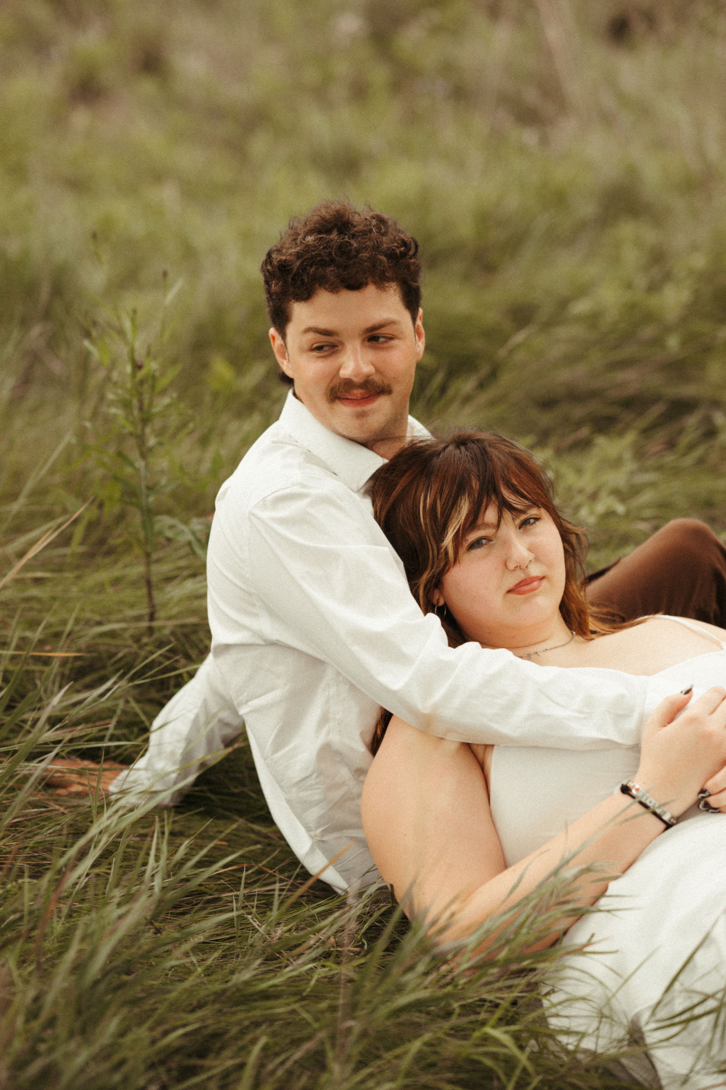 Lush green couples portrait featuring a woman in a white dress and a man in a white long sleeve shirt.