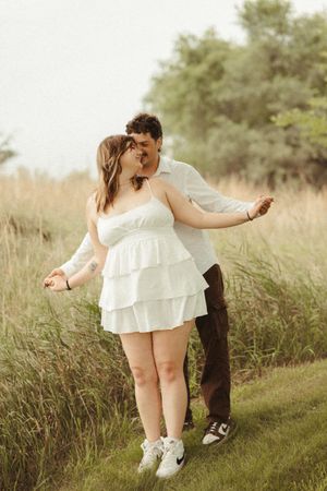 Couples photos of a woman in a white dress and a man in a white shirt with natural greenery and playful emotion.