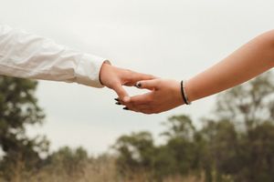 Outdoor couple session with young love, soft greenery and a warm, intimate portrait of hands touching.
