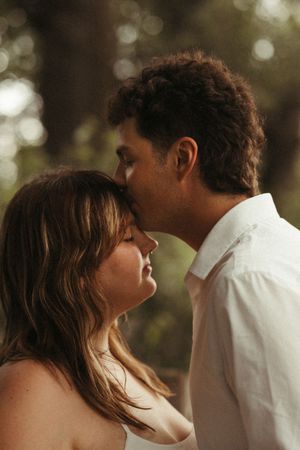 Romantic outdoor portrait of a couple dressed in white with soft greenery and an intimate, in-love feeling.
