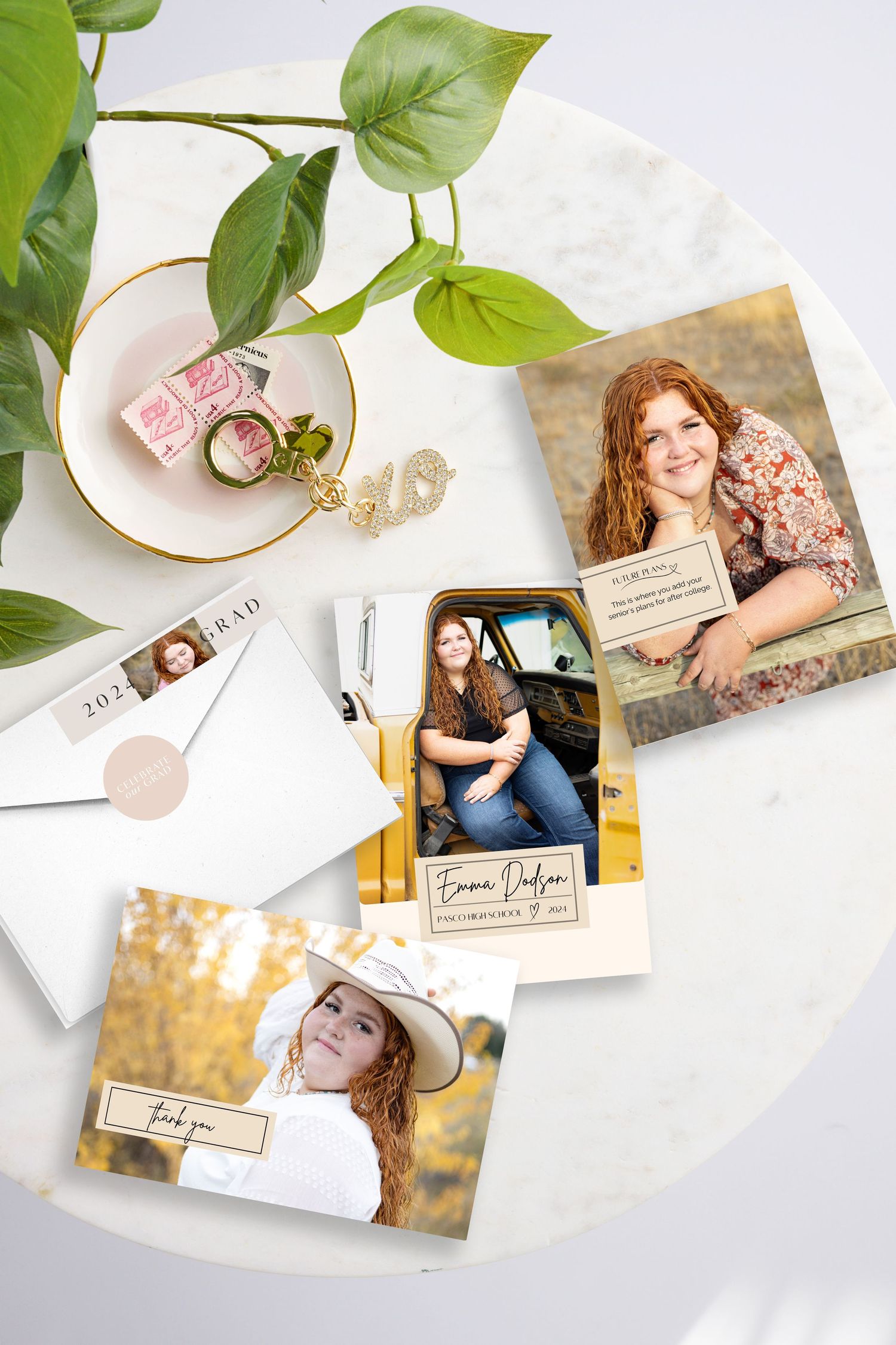 Graduation announcement cards featuring senior portraits of young women displayed on a marble table with jewelry and greenery.